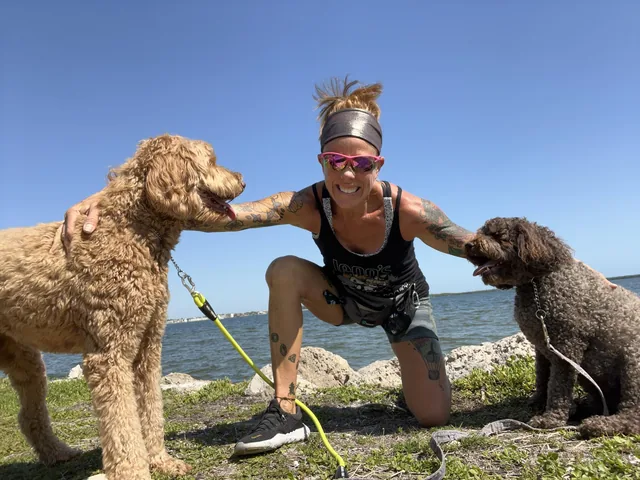 Jenn kneeling by the water with two doodles